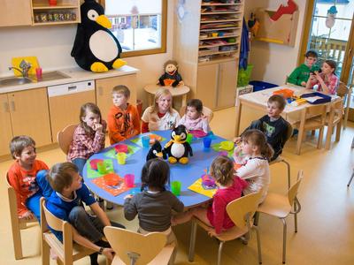 Kinder sitzen um einen Tisch im Kindergarten mit Spielzeugpinguinen in einem hellen Raum.