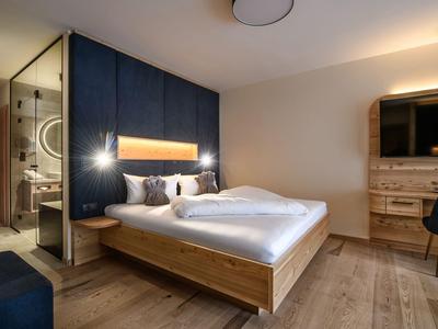 Modernes Hotelzimmer mit Holzdetails, Doppelbett, großem TV und offenem Badbereich.