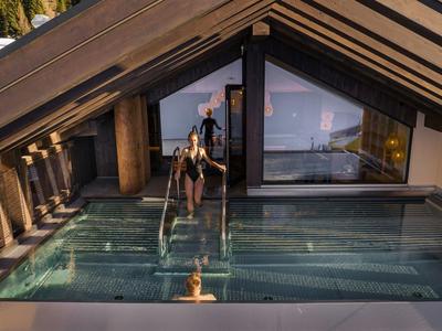 Eine Person steigt in einen modernen, überdachten Infinity-Pool mit Glaswänden, umgeben von Holzstrukturen.