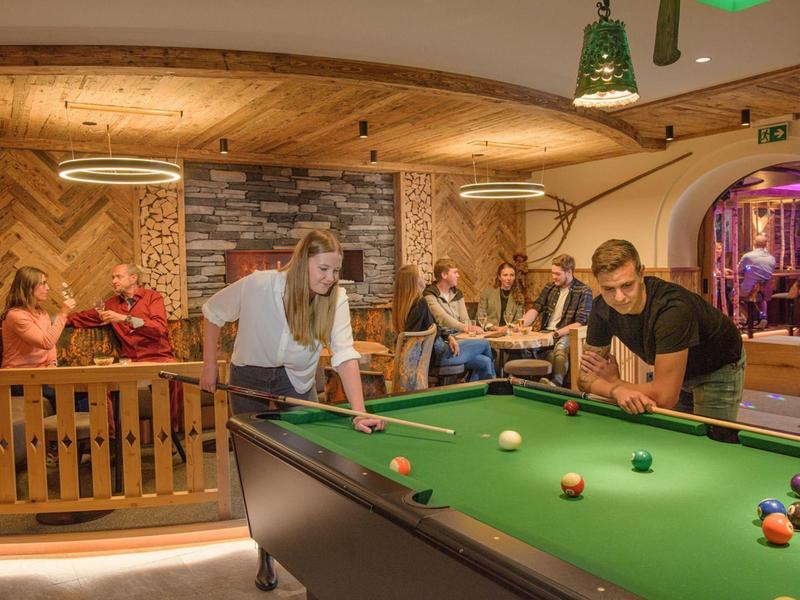 Menschen spielen Billard und entspannen in einer gemütlichen Lounge mit Holzvertäfelung.