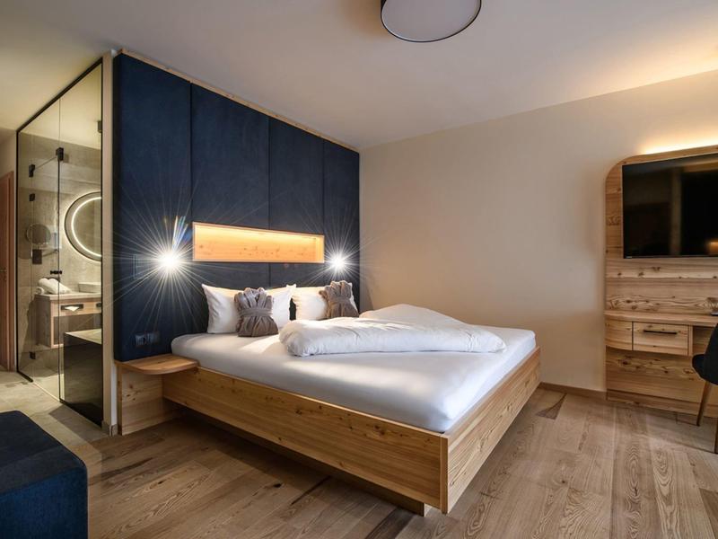 Modernes Hotelzimmer mit Doppelbett, Holzmöbeln und offenem Badbereich mit Glaswand.