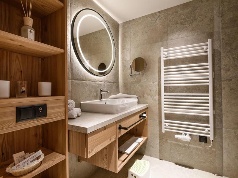 Modernes Badezimmer mit Holzregalen, rundem Spiegel und Waschtisch mit Waschbecken.