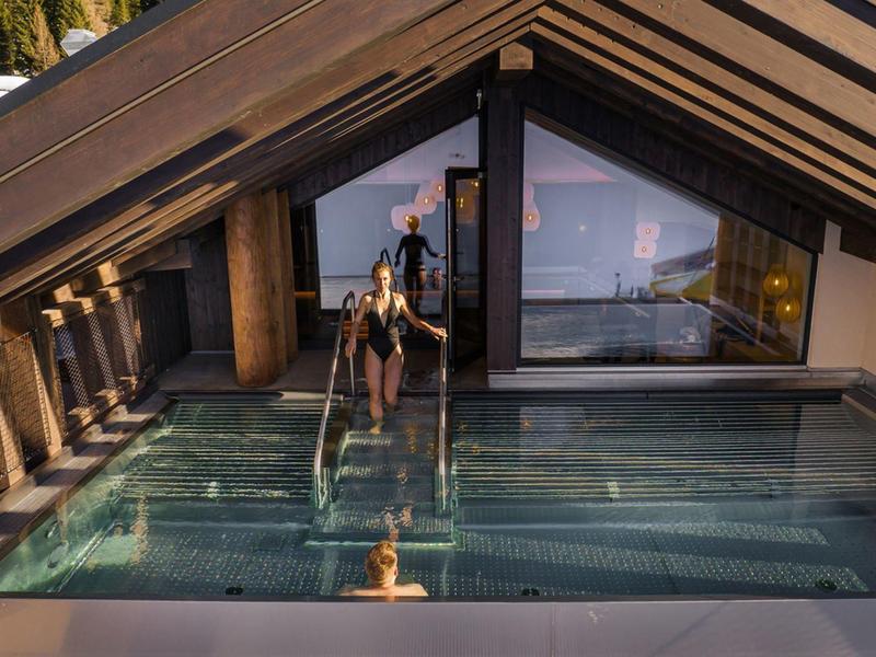 Person steigt aus einem überdachten Outdoor-Pool mit Bergblick bei Sonnenuntergang.