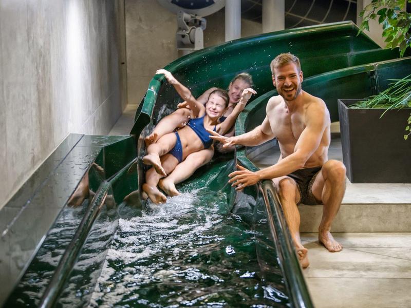 Drei Personen rutschen in einem Innenwasserrutschenbecken mit Spaß.