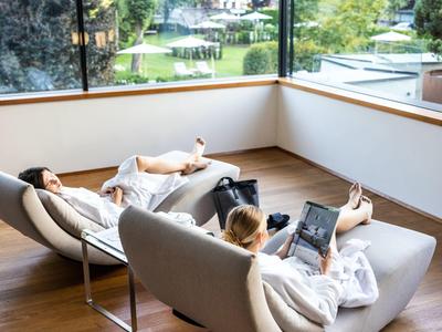 Zwei Personen entspannen in weißen Bademänteln auf modernen Sesseln mit Gartenblick.