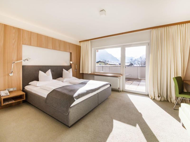 Helles Hotelzimmer mit Doppelbett, Holzverkleidung und Balkon mit Bergblick.