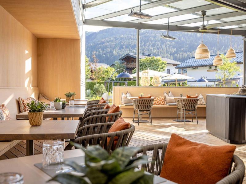 Gemütliche Hotelterrasse mit Tischen, Stühlen und Bergblick bei Sonnenschein.