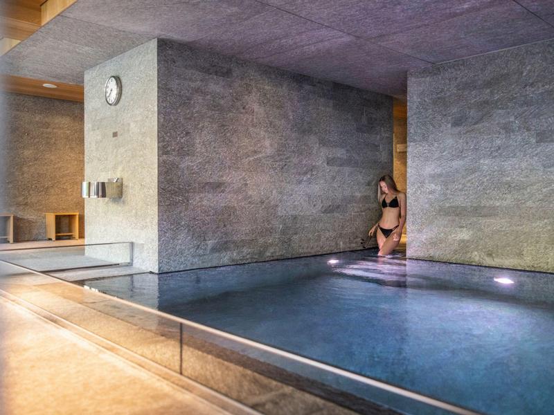 Frau sitzt am Rand eines modernen, innenliegenden Pools mit grauen Wänden.