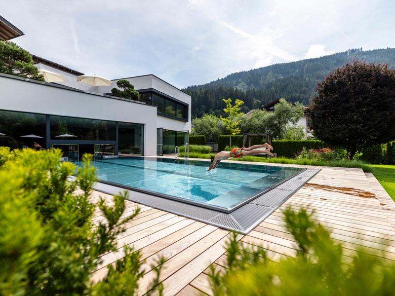 Moderner Pool mit Holzdeck und Bergblick neben einem weißen Hotelgebäude.