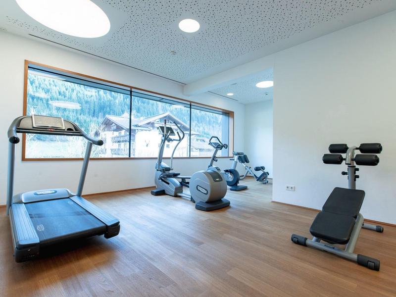Moderner Fitnessraum mit Laufband, Heimtrainer und Trainingsbank vor großen Fenstern.