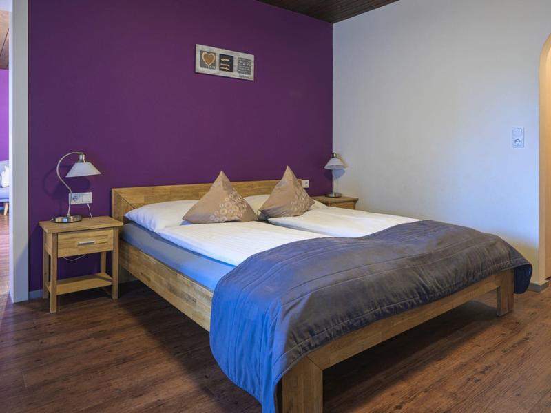 Schlafzimmer mit großem Bett, lila Wand und Holzboden in einem Hotelzimmer.