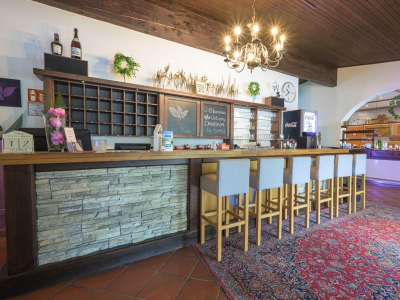 Hotelbar mit Holztheke, Polsterhockern und Teppichboden in warmem Ambiente.
