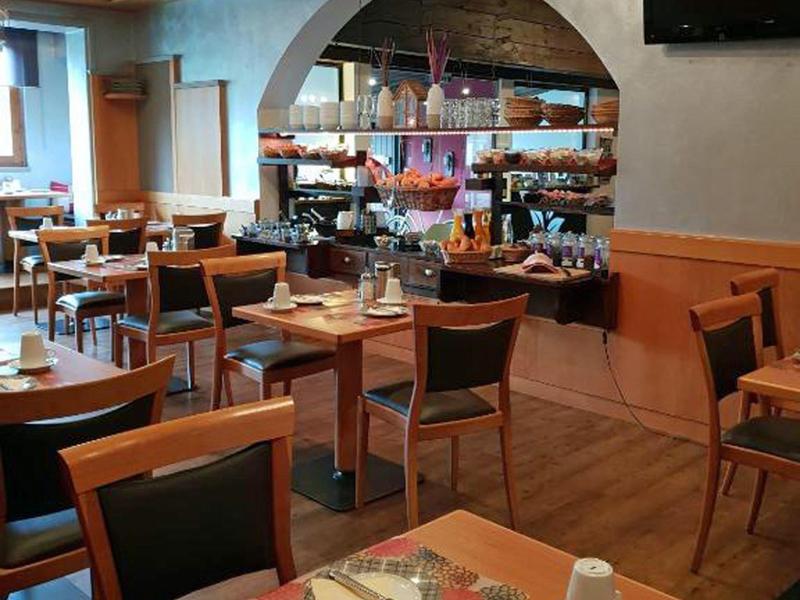 Gemütlicher Restaurantbereich mit Holzböden, Tischen und Stühlen sowie einem Spiegel an der Wand.