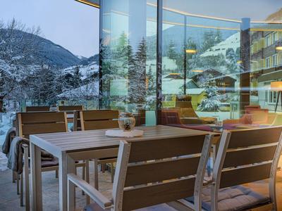 Terrasse mit Tischen und Stühlen vor einem modernen Hotel in verschneiter Berglandschaft.