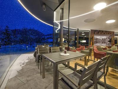 Moderne Hotellounge mit Tischen und Stühlen neben großen Fenstern mit Blick auf verschneite Landschaft.