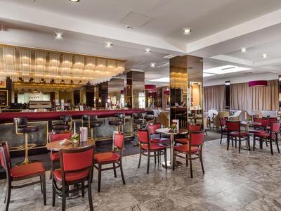 Großes Restaurant mit rot gepolsterten Stühlen und offener Bar in modernem Hotel.