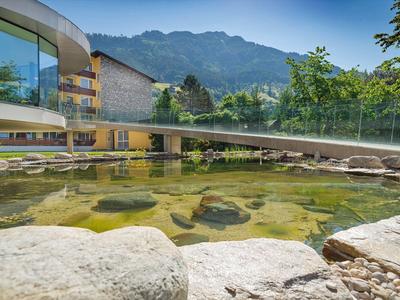 Moderner Hotelkomplex mit großem Teich und Bergpanorama im Hintergrund.