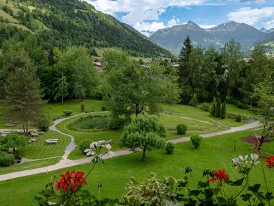 Grüne Berglandschaft mit gepflegtem Garten und gewundenen Wegen unter blauem Himmel.