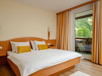 Helles Hotelzimmer mit Doppelbett, Holzmöbeln und Balkon mit Blick auf grüne Landschaft.