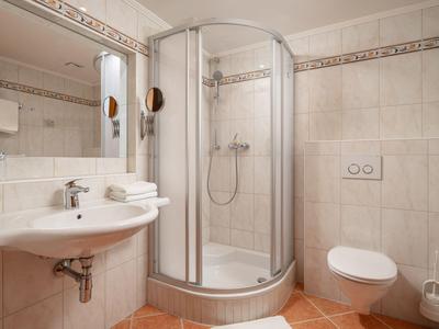 Helles Badezimmer mit Dusche, Waschbecken, Toilette und beigen Wandfliesen.