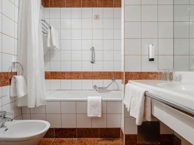Modernes Badezimmer mit weißem Fliesenmuster, Badewanne, Bidet und Waschbecken mit Handtüchern.