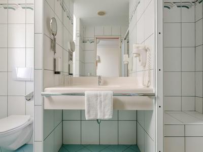 Helles Badezimmer mit weißen Fliesen, Waschbecken, Spiegel und Toilette.