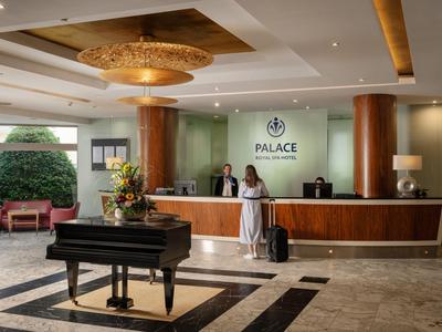 Moderner Hotel-Lobby mit Rezeption, großem Kronleuchter und schwarzem Flügel.