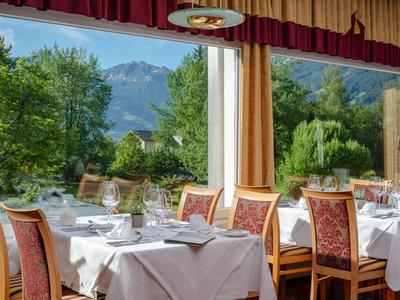 Ein Restaurant mit Tischen und Stühlen vor großen Fenstern mit Blick auf Bäume und Berge.