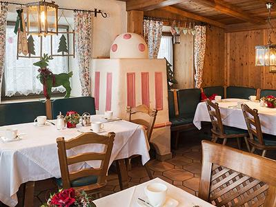 Ristorante accogliente con pareti in legno, tavoli apparecchiati e stufa a piastrelle tradizionale.