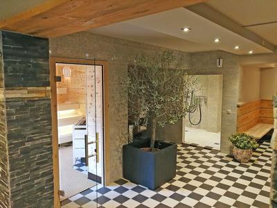 Interno di un hotel con pavimento a scacchi, piante e porte che conducono a una sauna.