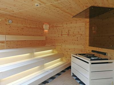 Interno di sauna in legno chiaro con panche a gradini e illuminazione moderna.