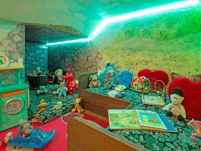 Area giochi colorata con giocattoli e libri in una camera d'hotel con illuminazione verde.