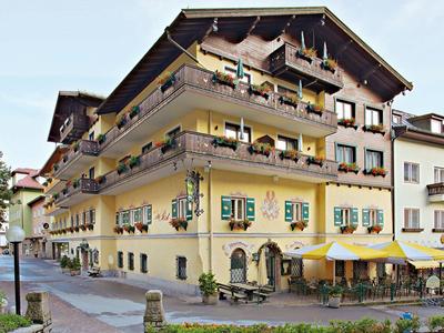 Traditionelles gelbes Hotelgebäude mit Holzbalustraden und Markisen an Fenstern und Terrasse.