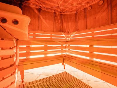 Holzsauna mit warmem orangefarbenem Licht und mehrstufigen Sitzbänken aus Holz.