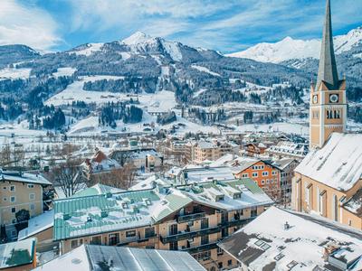 Winterliche Bergstadt mit verschneiten Dächern und Kirchturm vor schneebedeckten Bergen.