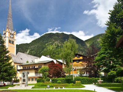 Dorf mit Kirche, bewaldeten Bergen und gepflegten Gärten bei klarem Himmel.
