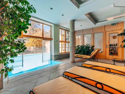 Innenbereich eines Wellnessbereichs mit Liegen, Pflanzen und Schwimmbecken mit Blick nach draußen.