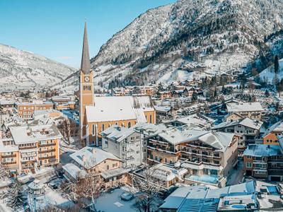 Verschneites Bergdorf mit Kirche und traditionellen Holzgebäuden unter klarem blauem Himmel.