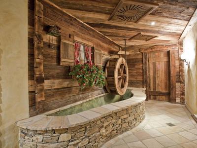Rustikaler Innenraum mit Steinbrunnen, Holzverkleidung und dekorativem Wagenrad an der Wand.