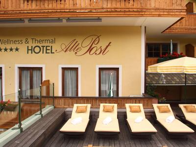 Hotelterrasse mit Liegestühlen und Sonnenschirm vor einer Fassade mit Hotelnamen.