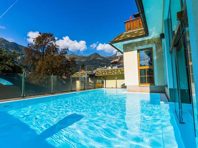 Moderner Hotelpool mit Bergblick und Glasgeländer bei sonnigem Himmel.