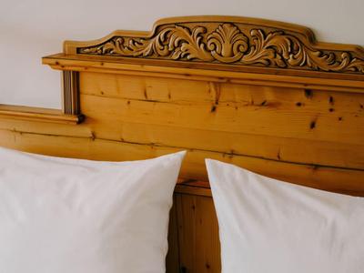 Bett mit geschnitztem Holzkopfteil und weißen Kissen in einem Hotelzimmer.