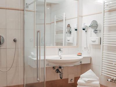 Helles Hotelbadezimmer mit Glasdusche, Waschbecken und Handtüchern.