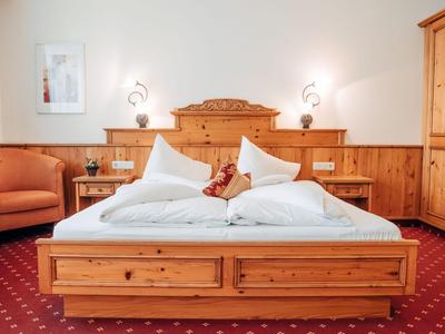 Gemütliches Hotelzimmer mit Holzmöbeln, Doppellbett, zwei Sesseln und rotem Teppich.