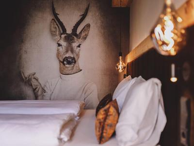 Hotelzimmer mit Bett und dekorativer Wand mit Hirschkopf und Antilope im Hintergrund.