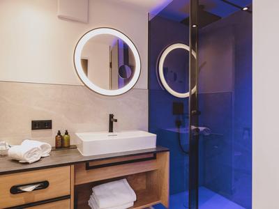 Moderner Hotelbadezimmer mit rundem beleuchtetem Spiegel und blauer Duschkabine.