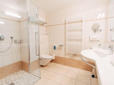 Helles Badezimmer mit Duschkabine, Wand-WC, Waschbecken und Handtuchheizung.