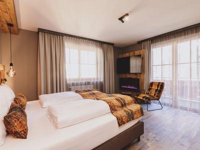 Modern eingerichtetes Hotelzimmer mit Doppelbett, Sessel und großem Fenster mit Vorhängen.