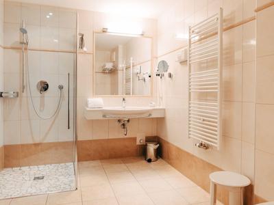 Modernes Badezimmer mit begehbarer Dusche, weißem Waschbecken und geräumigem Spiegel.