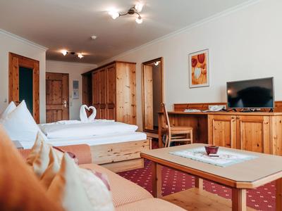 Hell eingerichtetes Hotelzimmer mit Holzmöbeln, Doppelbett und gemütlichem Sofa.